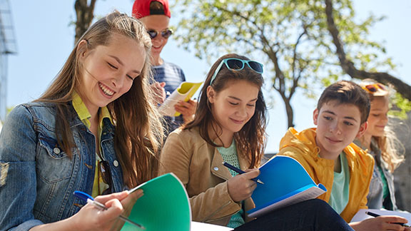 Schülerinnen und Schüler sitzen zusammen mit Heften in der Hand.